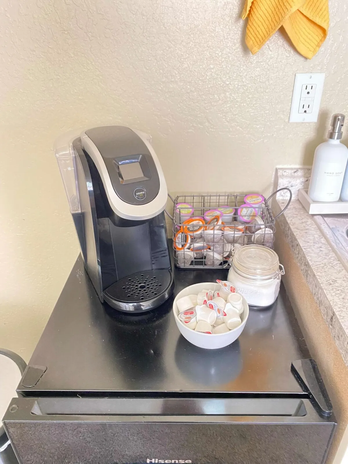 A cozy coffee corner with a coffee maker, creamers, sugar jar, and a dish towel neatly arranged. The inviting setup suggests moments of enjoying a fresh cup before embarking on city adventures.