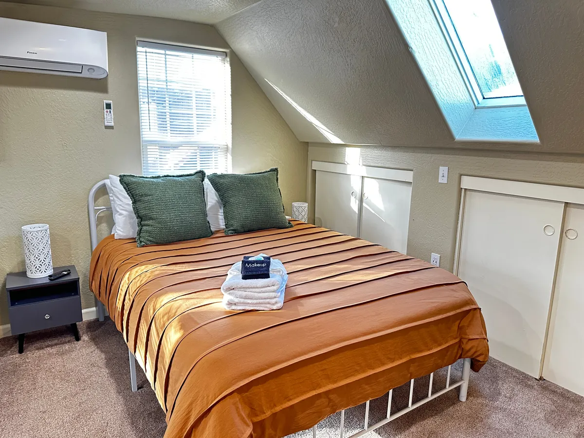 This image features a comfortable bed with an orange striped comforter and green decorative pillows, placed beneath a skylight. The scene is bathed in natural light, creating an inviting and restful atmosphere ideal for unwinding.