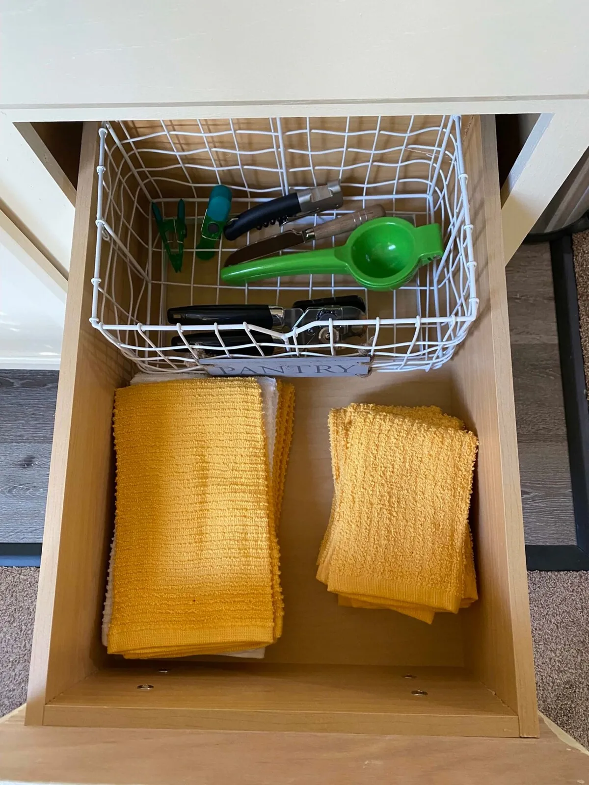 The image captures a practical kitchenette setup featuring yellow cloths, a wire basket, and various kitchen utensils neatly arranged. The area feels inviting and functional, ideal for cooking simple meals. Natural light and warm tones lend a homely, budget-friendly vibe.