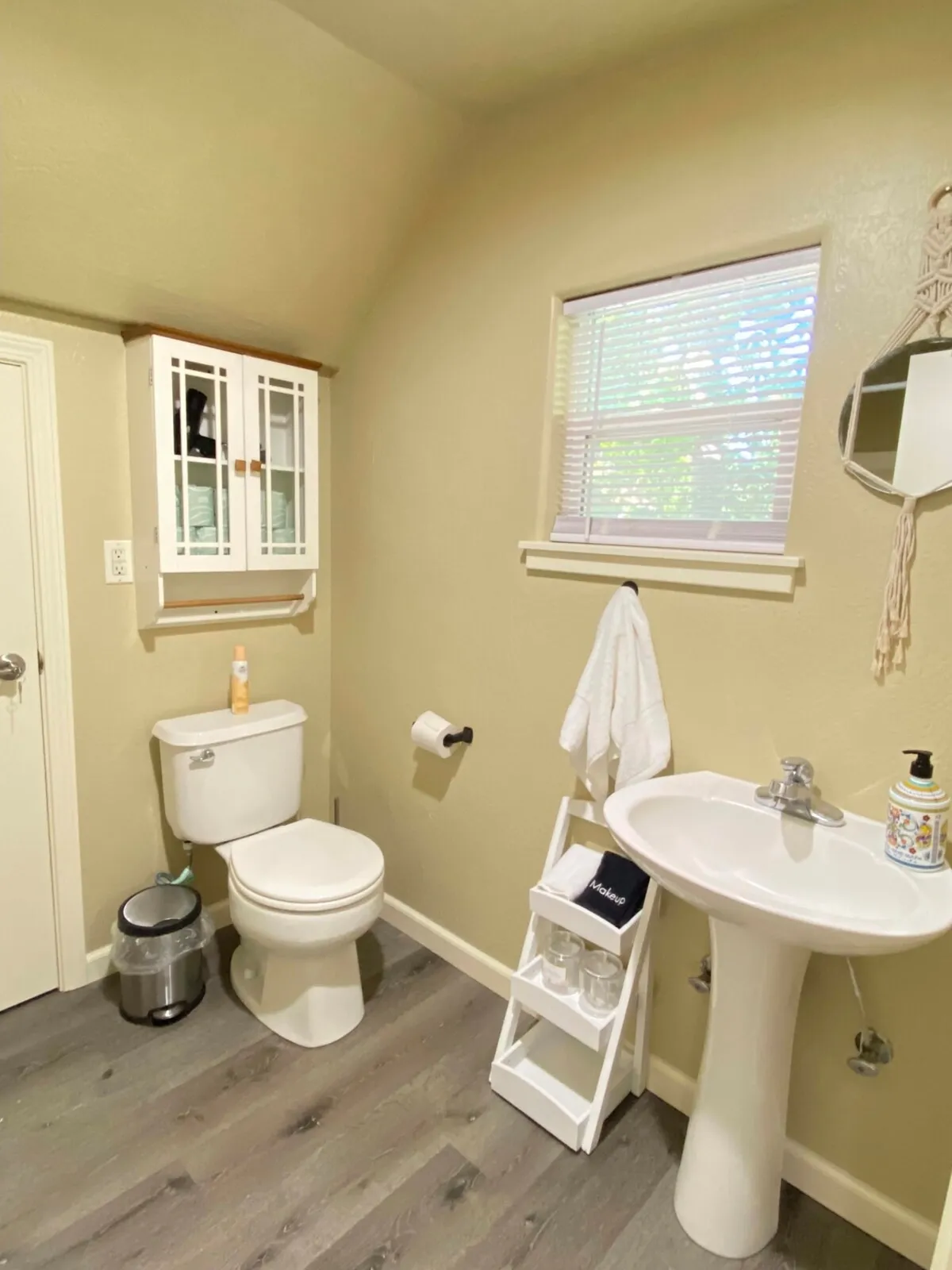 This image shows a clean, well-lit bathroom featuring a toilet, sink, mirrored cabinet, towel rack, and a window with blinds. The presence of a towel rack and mirrored storage highlights both functionality and comfort, while the window provides natural light for a refreshing atmosphere.