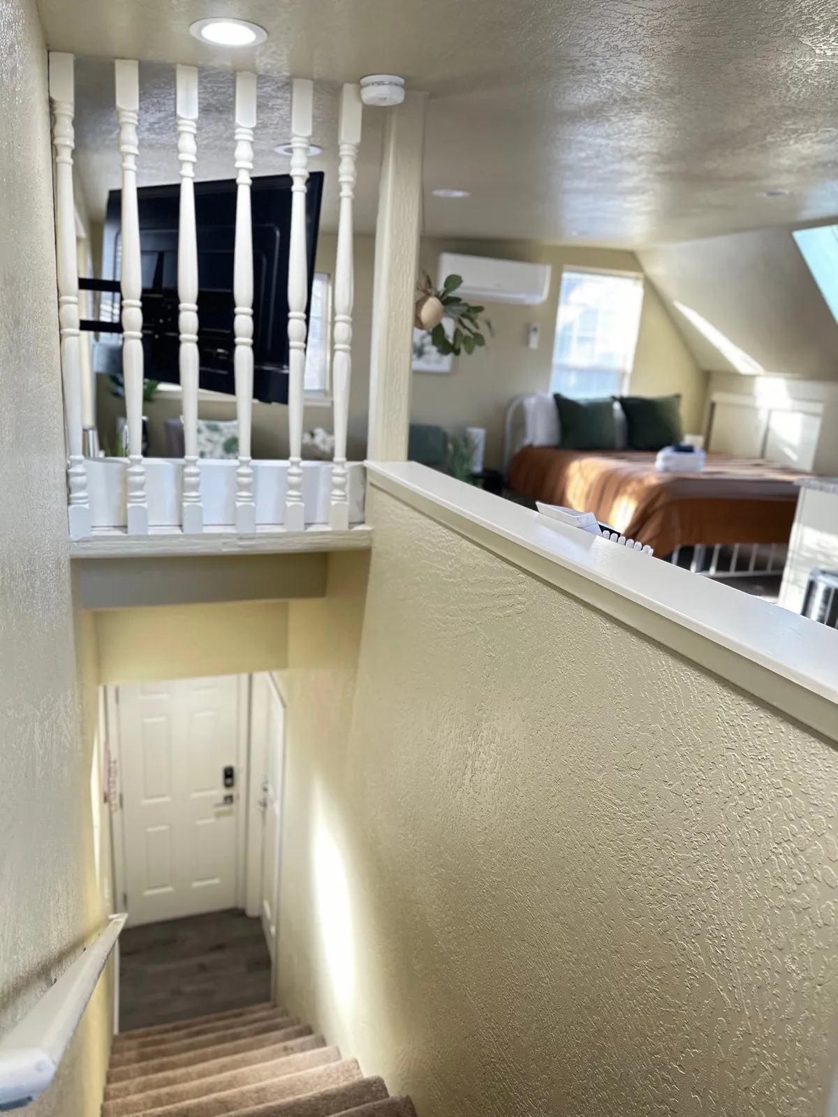 An interior perspective featuring a staircase and balustrade leading to the upstairs studio bedroom, bathed in natural window light. The photo conveys both access (the stairs) and the sense of privacy that comes with an upper-level unit.