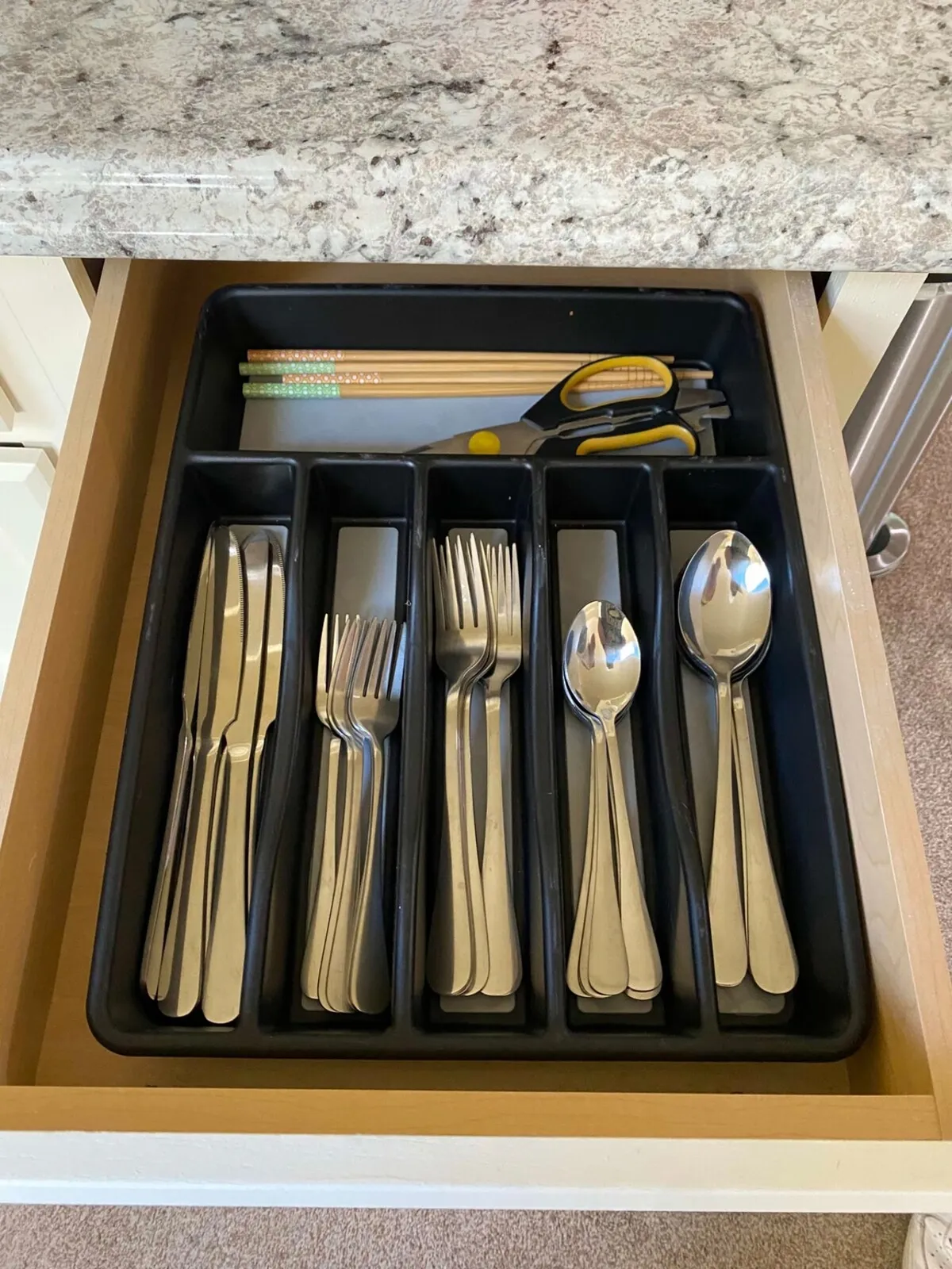 A functional kitchen area highlighted by a neatly arranged cutlery set, chopsticks, and scissors, all ready for meal preparation. The mood is practical and inviting, hinting at ease and convenience for quick meals or morning coffee.