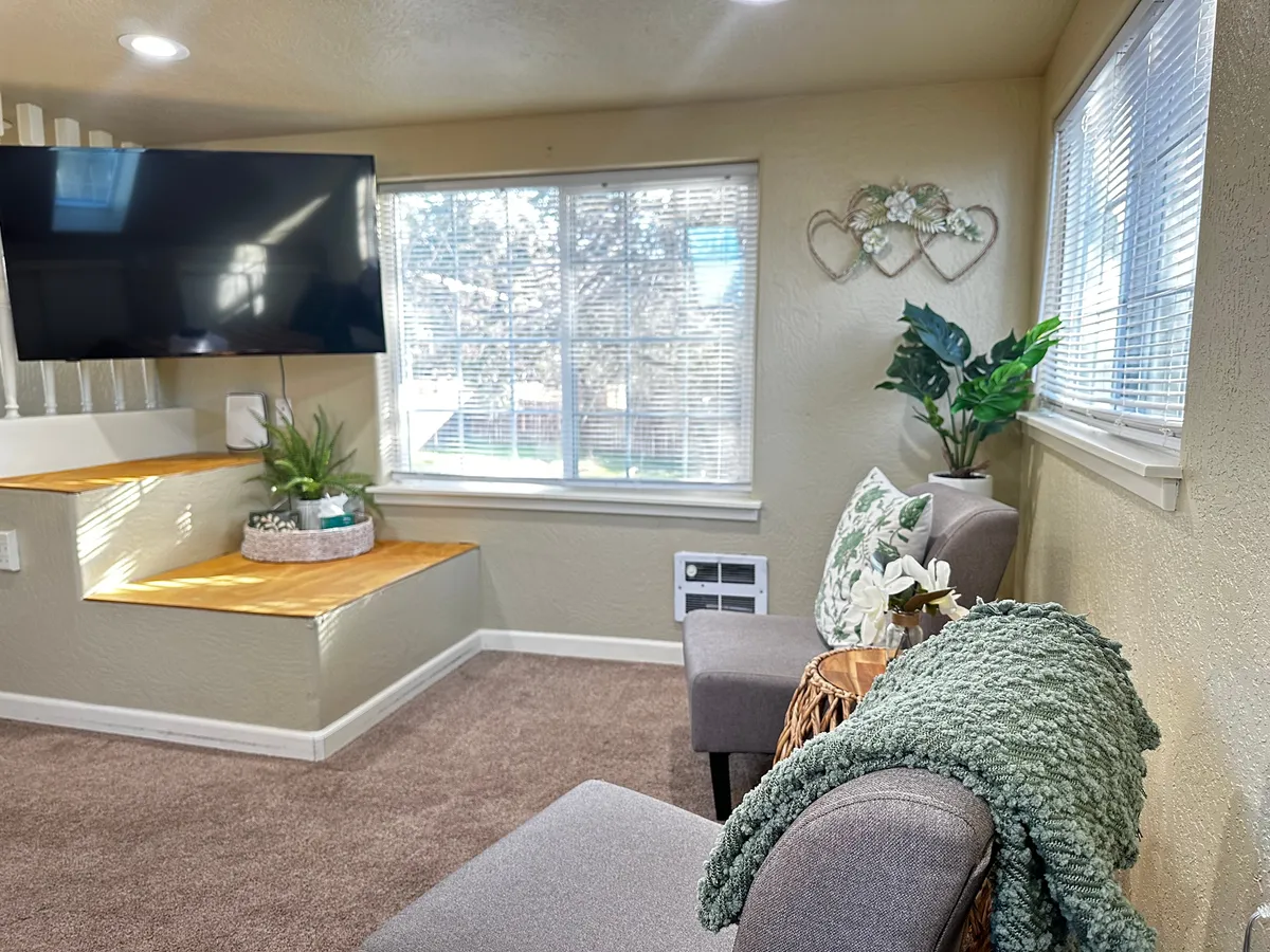 A cozy interior scene showcasing a comfortable seating area with a television, lush green plants, and charming decorative accents. The space invites relaxation and leisure, suggesting a private atmosphere perfect for unwinding or enjoying quiet moments.